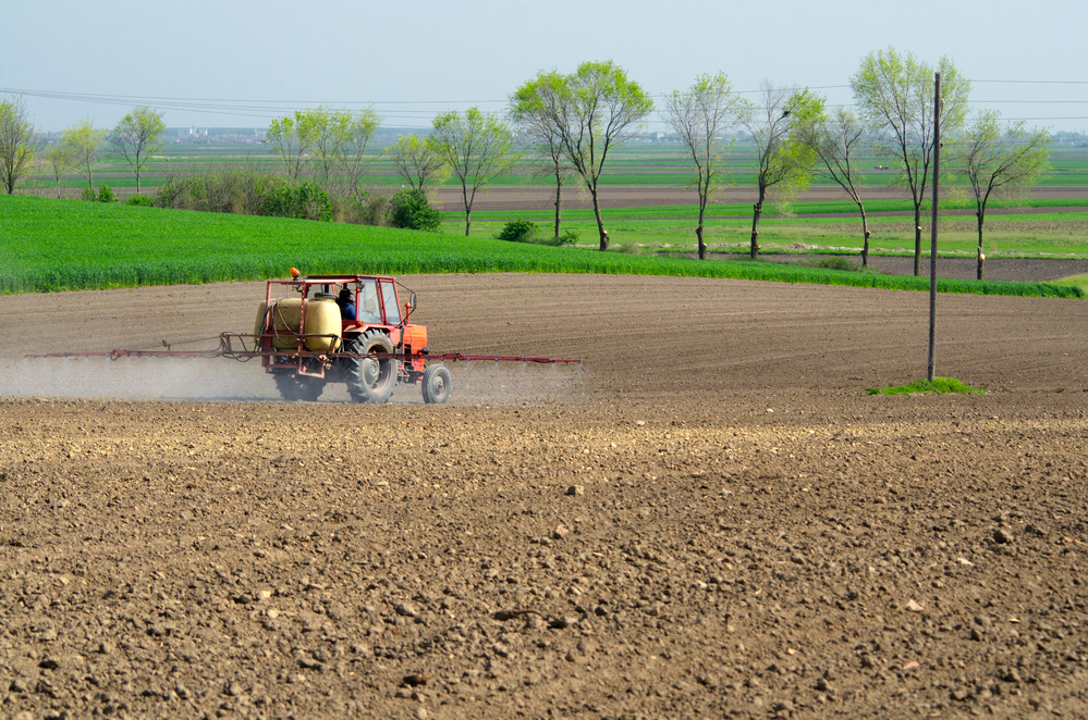 Tractor sprinkling pesticides againt bugs on plowed land on sunny spring day.