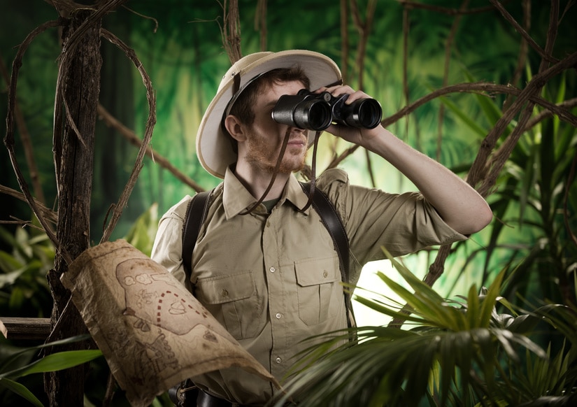 Expert explorer in the jungle looking away through binoculars.